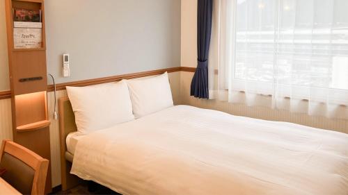 a white bed in a room with a window at Toyoko Inn Tsuruga Ekimae in Tsuruga