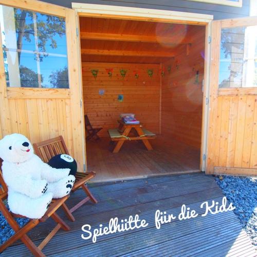 a bear sitting in a chair on the porch of a cabin at Ferienhaus Nordprinz mit Sauna und Whirlpool in Geestland