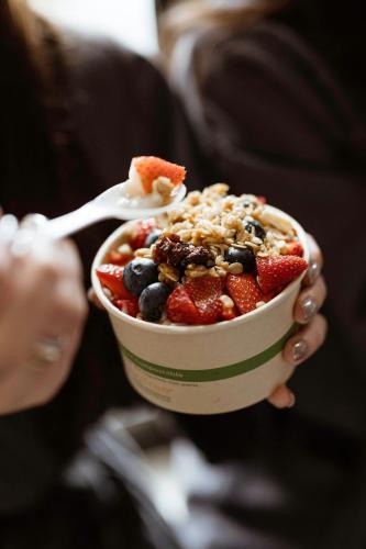 a woman holding a cup of fruit salad with a spoon at Boston Marriott Peabody in Peabody