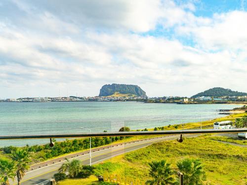 a road near the water with a mountain in the background at Jeju Attirance Hotel & poolvilla in Seogwipo