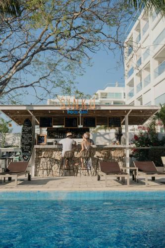 two people sitting at a bar next to a swimming pool at Santa Marta Marriott Resort Playa Dormida in Santa Marta