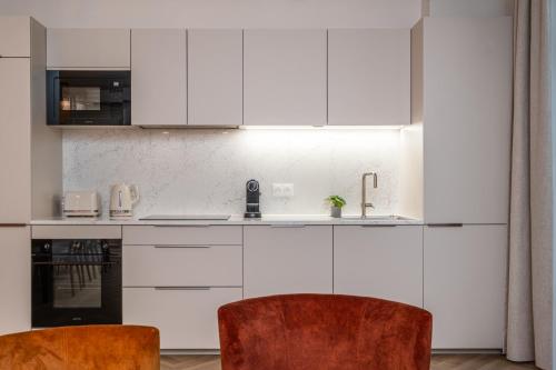 a white kitchen with white cabinets and two chairs at L'Horloge - Appart'Hotel proche de Disneyland in Montévrain