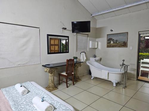 a bathroom with a tub and a bed and a desk at Tzaneen White House Lodge in Tzaneen
