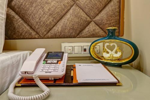 a phone on a table with a book and a vase at The Viking Hotel- 5 Minutes away from New Delhi Railway & Connaught Place in New Delhi