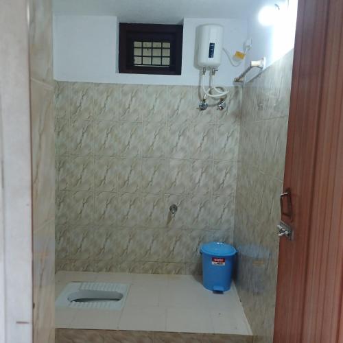 a bathroom with a shower with a blue trash can at THEERTHAMKARA Staycation in Nīleshwar