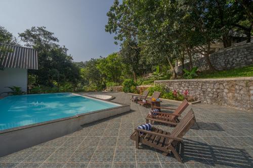 a swimming pool with two wooden chairs next to it at SaffronStays Raanwaara Luxe in Āmbavna
