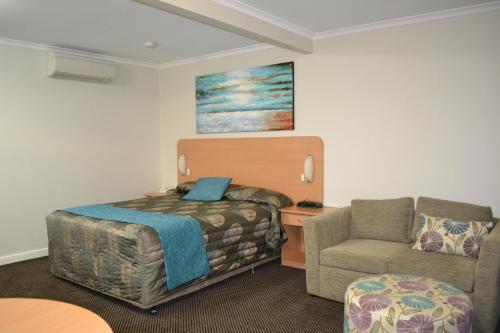 a hotel room with a bed and a chair at Cattlemans Country Motor Inn & Serviced Apartments in Dubbo