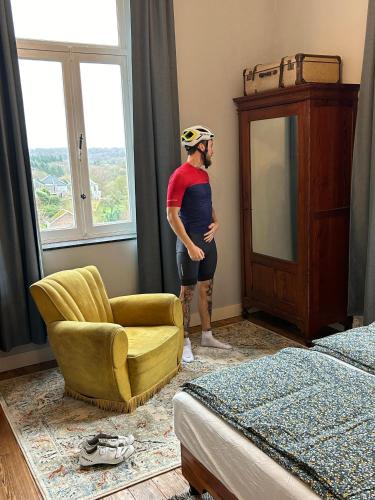 a man is standing in a bedroom with a chair and a window at La Maison Vienvenue - Bike, hike and meet alike in Anthisnes