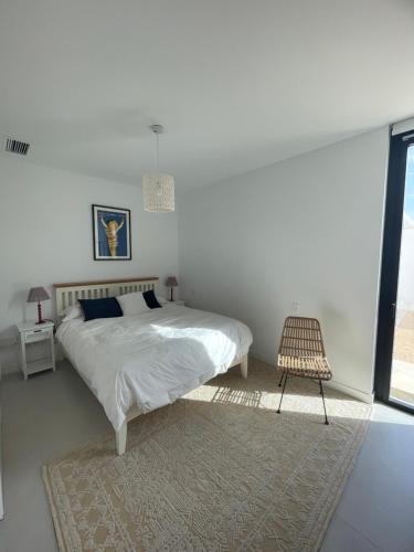 ein weißes Schlafzimmer mit einem Bett und einem Stuhl in der Unterkunft Hostidy Villa Horacia Resort in Sanlúcar de Barrameda