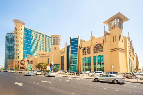 Grand Millennium Al Wahda Hotel and Executive Apartments Abu Dhabi في أبوظبي: شارع المدينة فيه سيارات تقف امام مبنى