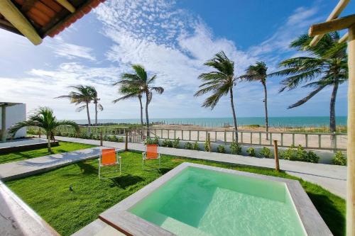 a swimming pool with palm trees and the ocean at The Point Bangalô Pé na Areia em Fortim in Fortim