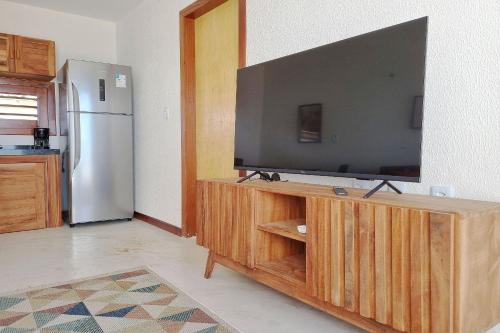 a television on a wooden stand in a kitchen with a refrigerator at The Point Bangalô Pé na Areia em Fortim in Fortim