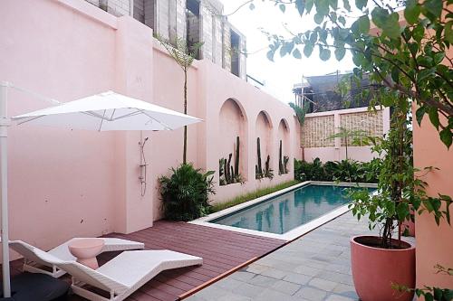 a swimming pool with a white umbrella and a chair at Ponder Bali Canggu in Canggu