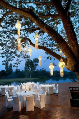 a banquet hall with white tables and chairs under a tree at Le Meridien Chiang Rai Resort, Thailand in Chiang Rai