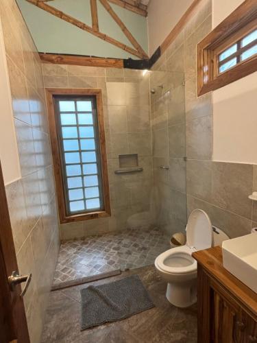 a bathroom with a toilet and a shower with a window at Sirena's Beach & Surf Club in Canoa
