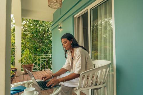 a woman sitting in a chair using a laptop on a porch at Bleu de Toi Boutique Hotel in Grand Baie