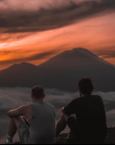 two people sitting on top of a mountain at sunset at Pondok Bulan Lake View in Kintamani