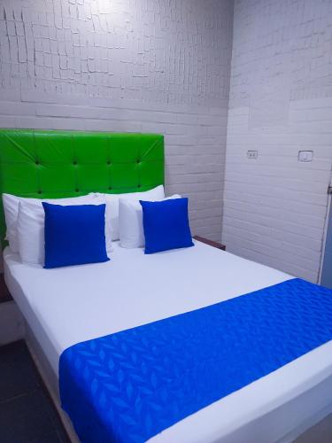 a large bed with blue pillows and a green headboard at Hotel Casa Boston Inn by Finerh in Barranquilla
