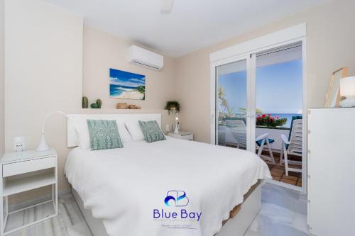 a white bedroom with a white bed and a balcony at Bliss On The Bay Apartment in La Herradura