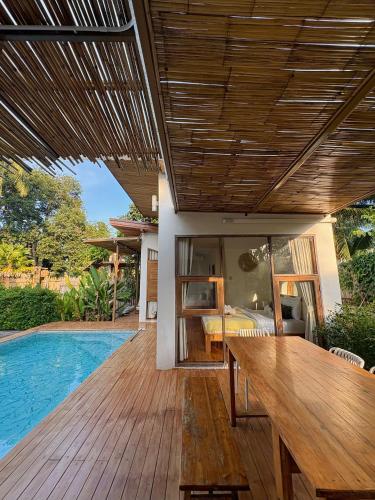 a wooden deck with a table next to a swimming pool at บ้านพราวพร้าว Baan Proud Proud in Khanom