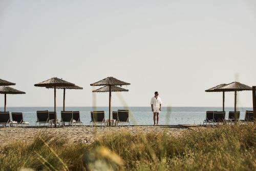 a man standing on a beach with chairs and umbrellas at Myrion Beach Resort & Spa - Adults Only in Gerani Chanion