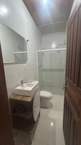 a bathroom with a sink and a toilet and a mirror at Casa 3 quartos com Piscina no centro de Penha - SC in Penha