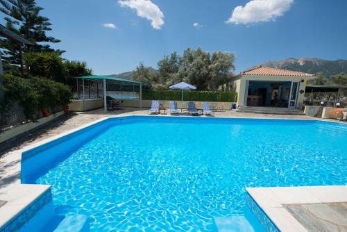 a large blue swimming pool with chairs and a house at Ilios Hotel & Villas in Yenion