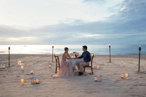 a bride and groom sitting at a table on the beach at Sheraton Hua Hin Resort & Spa in Cha Am