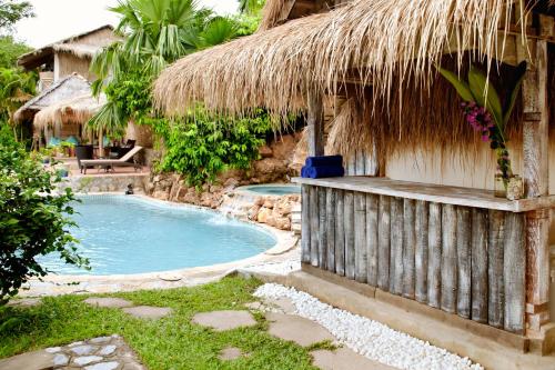 un complejo con una piscina y una cabaña de paja en The Beach House, en Kep