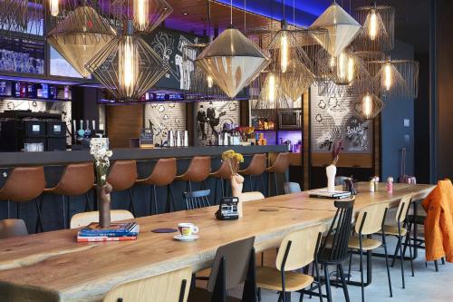 a large table in a restaurant with chairs and lights at Moxy Birmingham NEC in Bickenhill