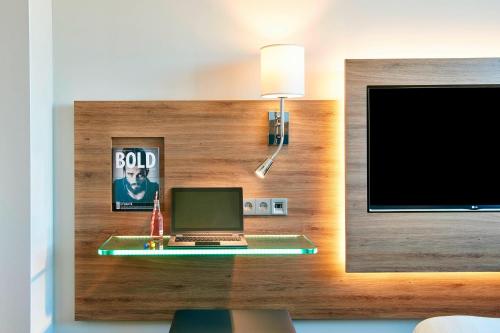 a desk with a laptop and a television on a wall at Moxy London Stratford in London