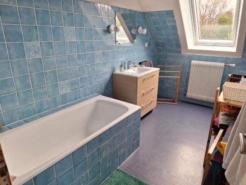 La salle de bains est pourvue de carrelage bleu, d'une baignoire et d'un lavabo. dans l'établissement LàTeLier22, à Le Foeil