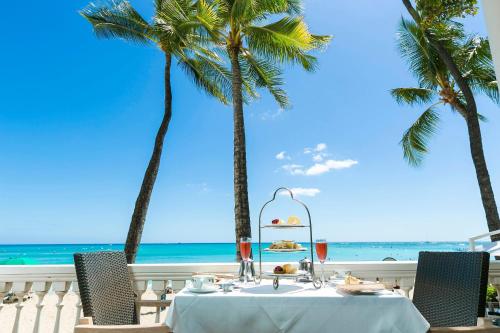 a table on the beach with palm trees and the ocean at Moana Surfrider, A Westin Resort & Spa, Waikiki Beach in Honolulu