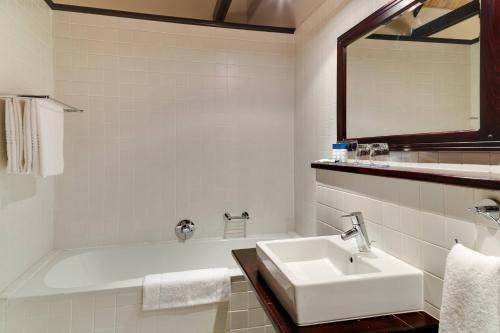 a white bathroom with a sink and a bath tub at Protea Hotel by Marriott Dorpshuis & Spa Stellenbosch in Stellenbosch