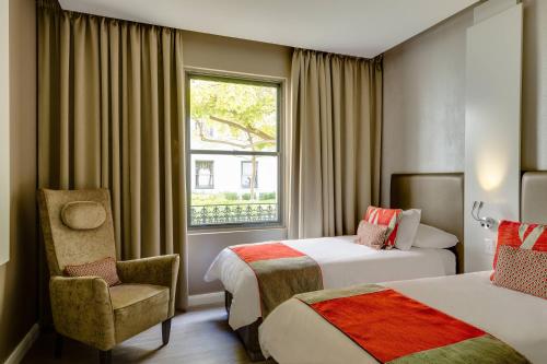 a hotel room with two beds and a chair and a window at Protea Hotel by Marriott Cape Town Waterfront Breakwater Lodge in Cape Town