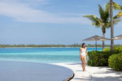 a woman in a white bikini walking down a path by the ocean at The Ritz-Carlton Maldives, Fari Islands in North Male Atoll
