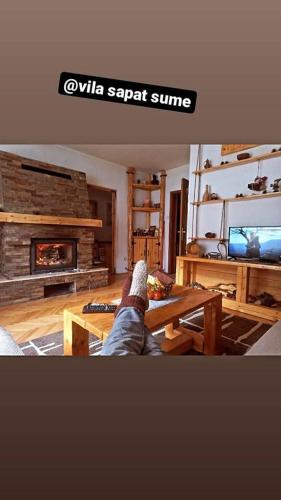 a persons feet on a table in a living room with a fireplace at Vila Šapat šume in Ljuboš