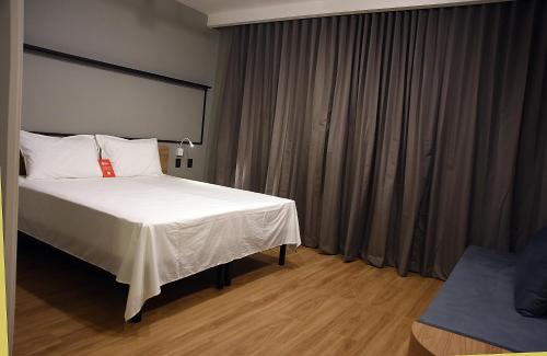 a bedroom with a large bed with white sheets at ibis Tangará Da Serra in Tangara da Serra