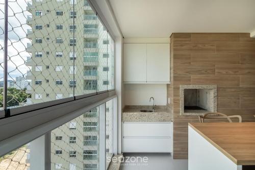 a kitchen with white cabinets and a large window at Condomínio a beira-mar c/ piscina - SHC in Piçarras