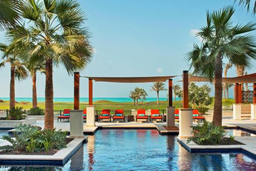 a swimming pool with palm trees and chairs at The St. Regis Saadiyat Island Resort, Abu Dhabi in Abu Dhabi