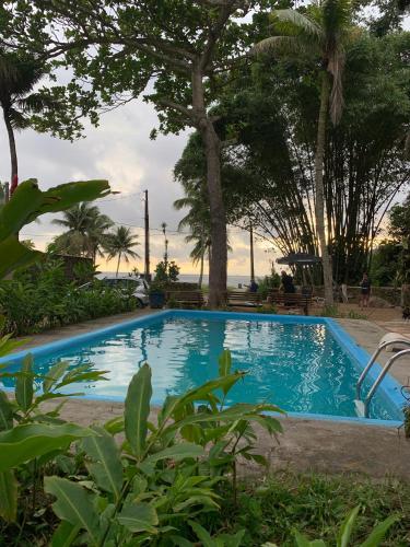 a blue swimming pool with trees in the background at Frente ao Mar - Suites com Piscina Aquecida, SPA Privativo, Vista ao Mar ou Montanha, com Estacionamento- Raizes do Mar ECO Hotel in Guarujá