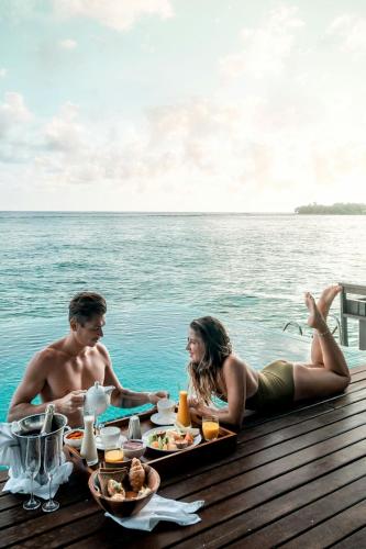 a man and woman sitting at a table in the water at Sheraton Maldives Full Moon Resort & Spa in North Male Atoll