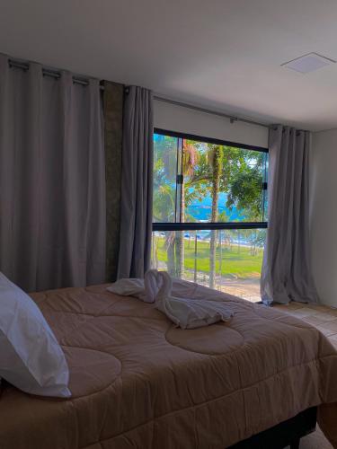 a bedroom with a bed and a large window at Frente ao Mar - Suites com Piscina Aquecida, SPA Privativo, Vista ao Mar ou Montanha, com Estacionamento- Raizes do Mar ECO Hotel in Guarujá