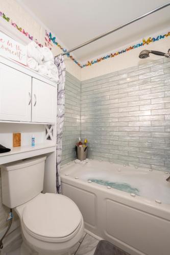 a white bathroom with a tub and a toilet at Arcade, Ping Pong, Hot Tub, Gas Grill, & King Bed in Kernersville