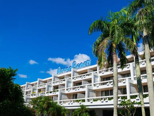 a large white hotel with palm trees in front of it at The Moon Beach Museum Resort in Onna