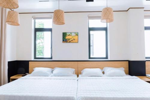 two beds in a bedroom with two windows at Nami Homestay in HÆ°ng YÃªn