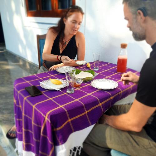 a woman sitting at a purple table with a plate of food at Eco Rich Villa in Pamunugama
