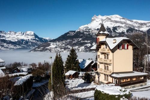une maison dans la neige avec des montagnes en arrière-plan dans l'établissement Villa la tourelle, à Saint-Gervais-les-Bains