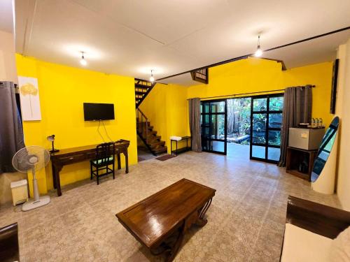 a living room with yellow walls and a wooden table at Baibon3 Homestay Thalang Phuket in Ban Na Nai