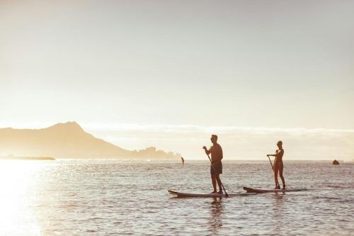 three people standing on paddle boards in the water at The Ritz-Carlton Residences, Waikiki Beach Hotel in Honolulu